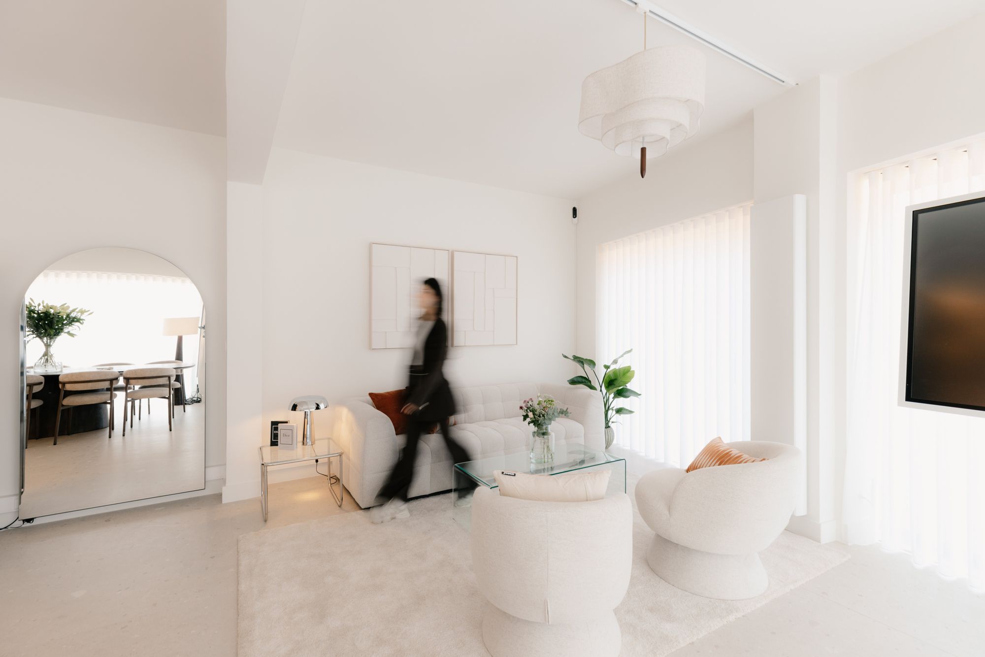 Iemand wandelt door de lichte loungehoek van The Social Studio met gebogen spiegel en witte fauteuils